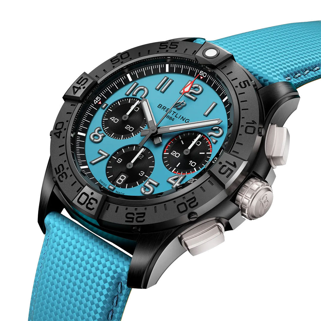 A close-up of the BREITLING Avenger B01 Chronograph 42 Night Mission shows a black case, turquoise dial, three black subdials, textured turquoise strap, bold black bezel numerals, and white and red hands. Brand: Breitling.