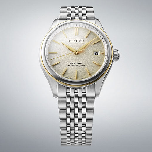 The Seiko Presage Classic Series Automatic 40.2mm Watch features a silver textured dial, gold hour markers and hands, a date window at 3 o'clock, a stainless steel bracelet, and a bezel with a subtle gold accent.