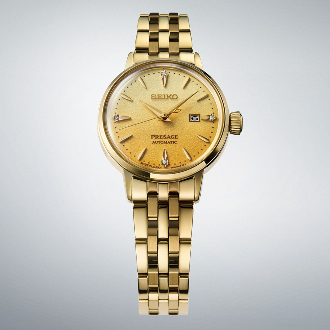 The Seiko Presage Cocktail Time Automatic with Manual Winding 30.3mm Watch features a gold round dial, gold markers, date display, and a gold metal link bracelet, shown against a light gradient background.