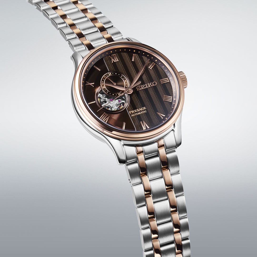 The Seiko Presage Japanese Garden Automatic with Manual Winding 41.8mm Watch features a two-tone silver and rose gold metal band, black patterned dial, rose gold Roman numerals, and an open-heart complication.