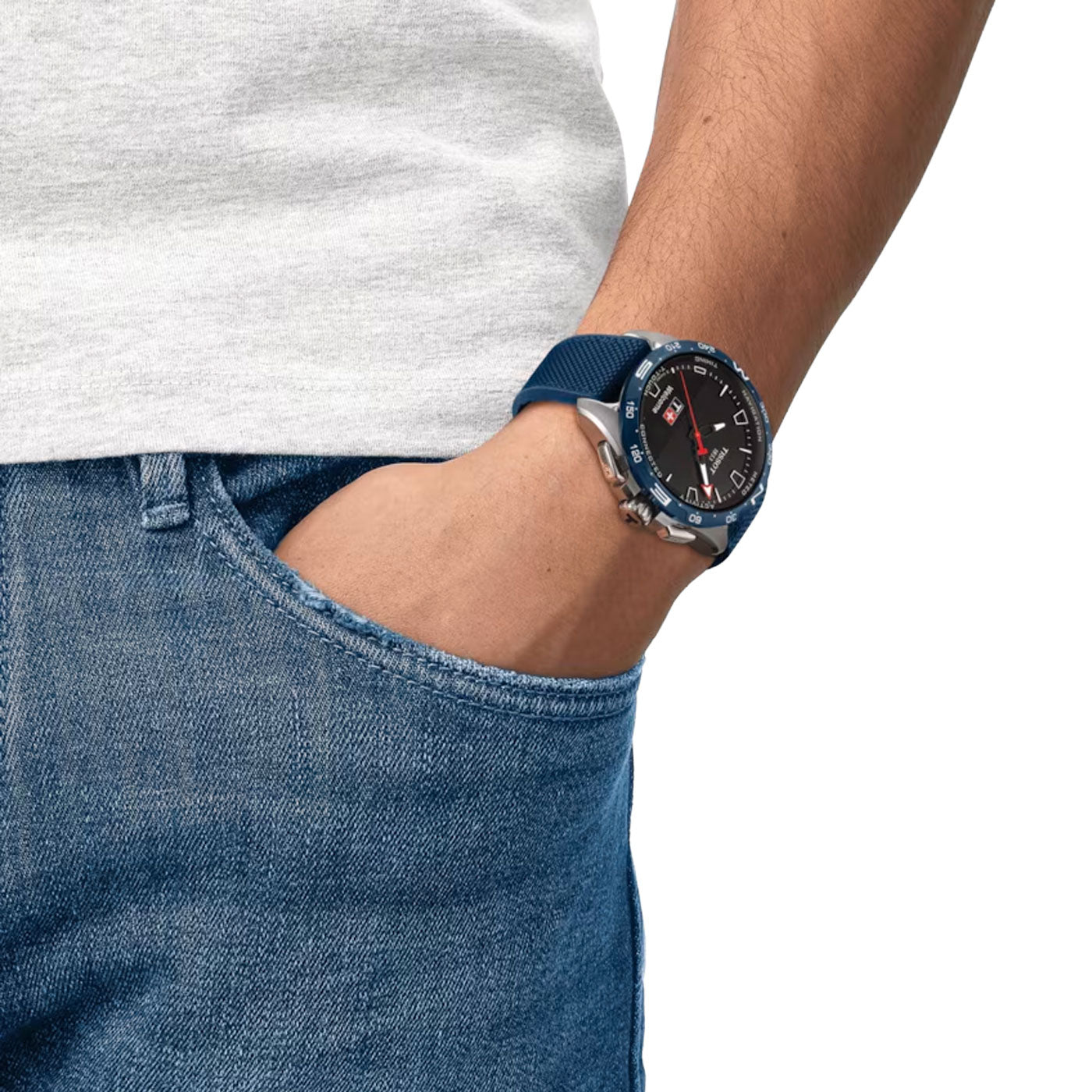 A person in a white t-shirt and blue jeans is wearing a Tissot T-Touch Connect Solar Quartz 47.5mm Smart Watch on their left wrist. The timepiece, with its Swiss connected quartz movement and round black dial, features a silver and blue design. Its sapphire crystal glistens as the person's left hand rests in their jeans pocket.