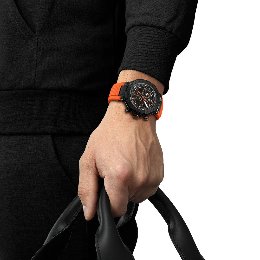 Wearing a Tissot T-Race Chronograph Quartz 45mm Watch by Tissot with an orange band, a person in black holds black handles. The watch’s detailed chronograph face features multiple dials on a crisp white background.