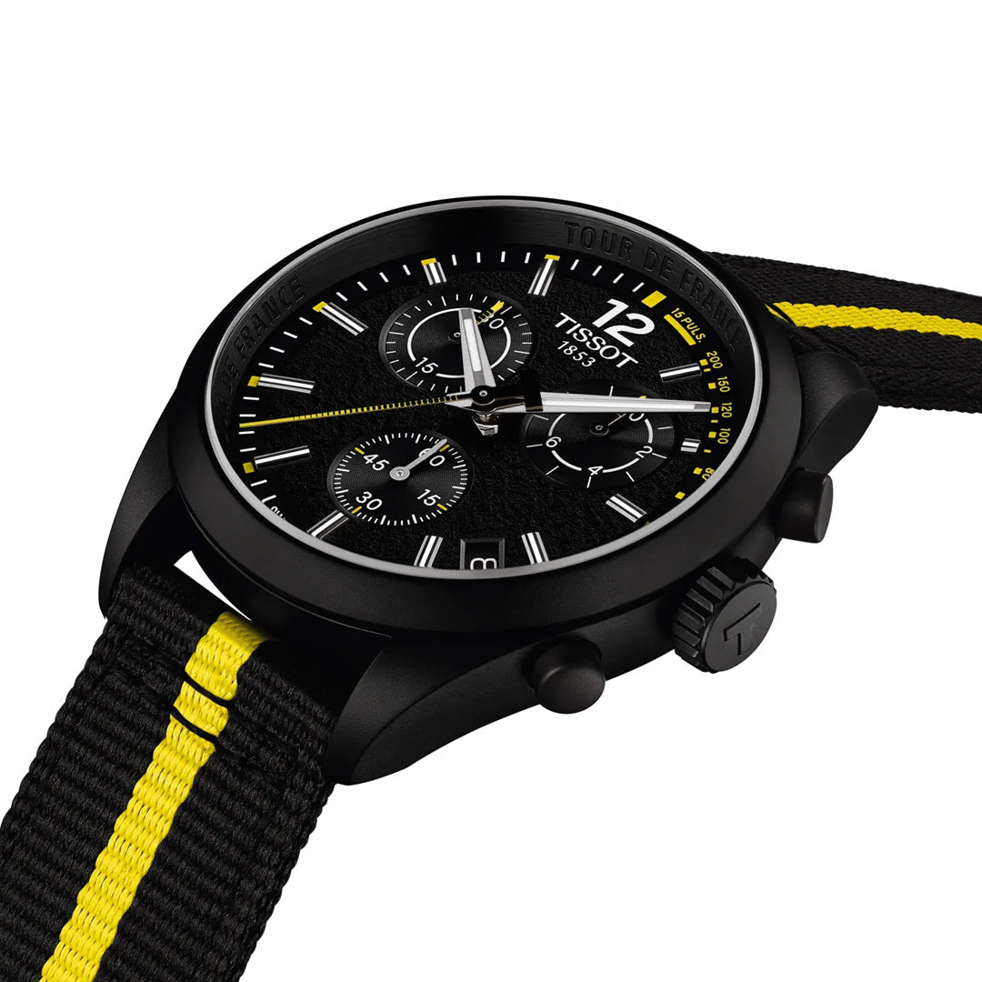 The Tissot PR100 Chronograph Tour De France 2026 Quartz 40mm Watch features a black and yellow striped nylon strap, a black dial with white and yellow markers, and three subdials. The timepiece is displayed at an angle on a white background.