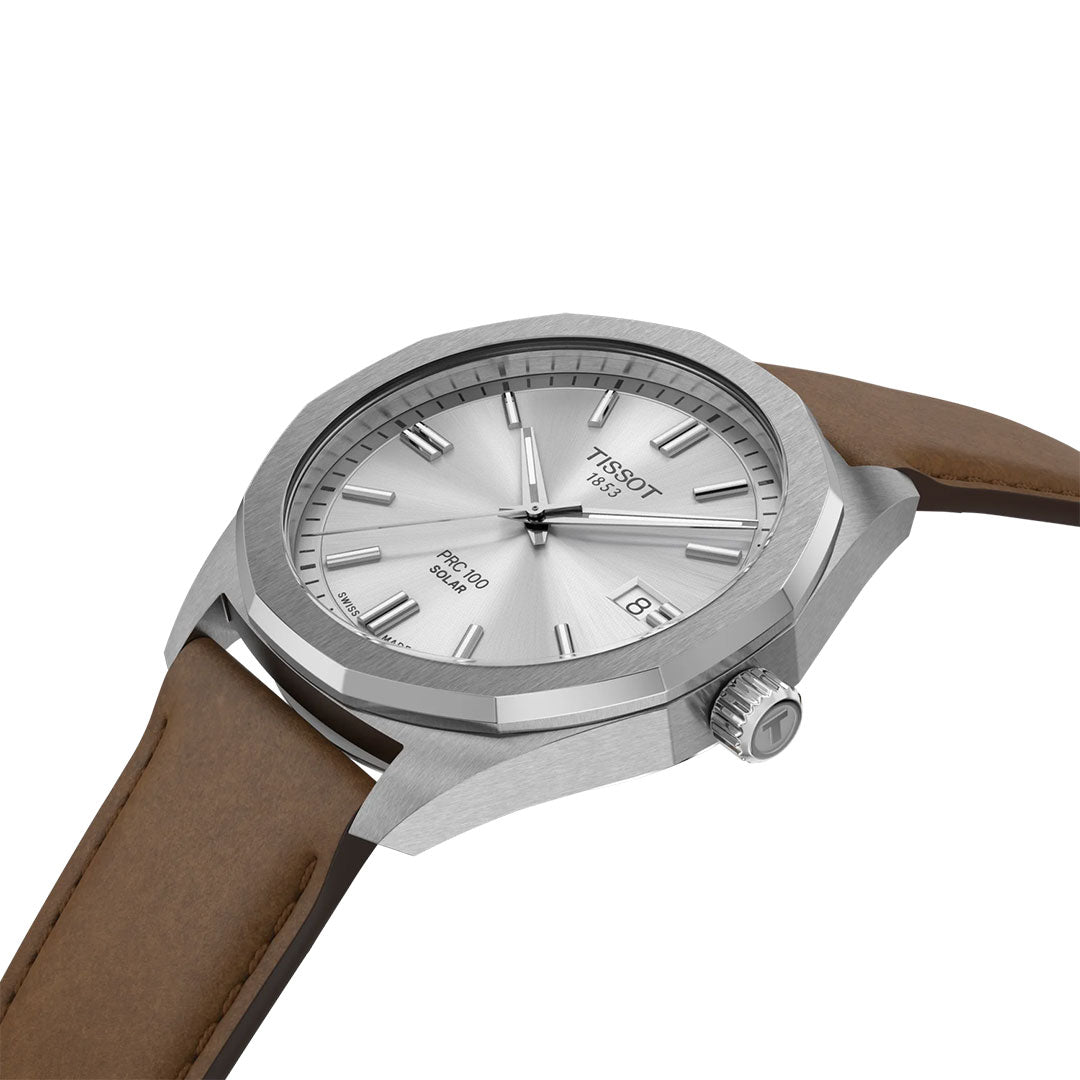 The Tissot PRC 100 Solar Quartz 39mm Watch features a silver case, brown leather strap, silver dial with minimalist markers, and a date display at 3 o’clock, displayed at an angle on a white background.