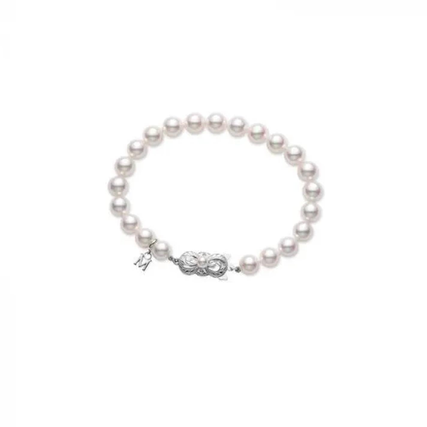 A strand of lustrous Akoya cultured pearls forms a bracelet featuring an elegant 18K white gold clasp from Mikimoto, beautifully arranged in a circle on a plain white background.
