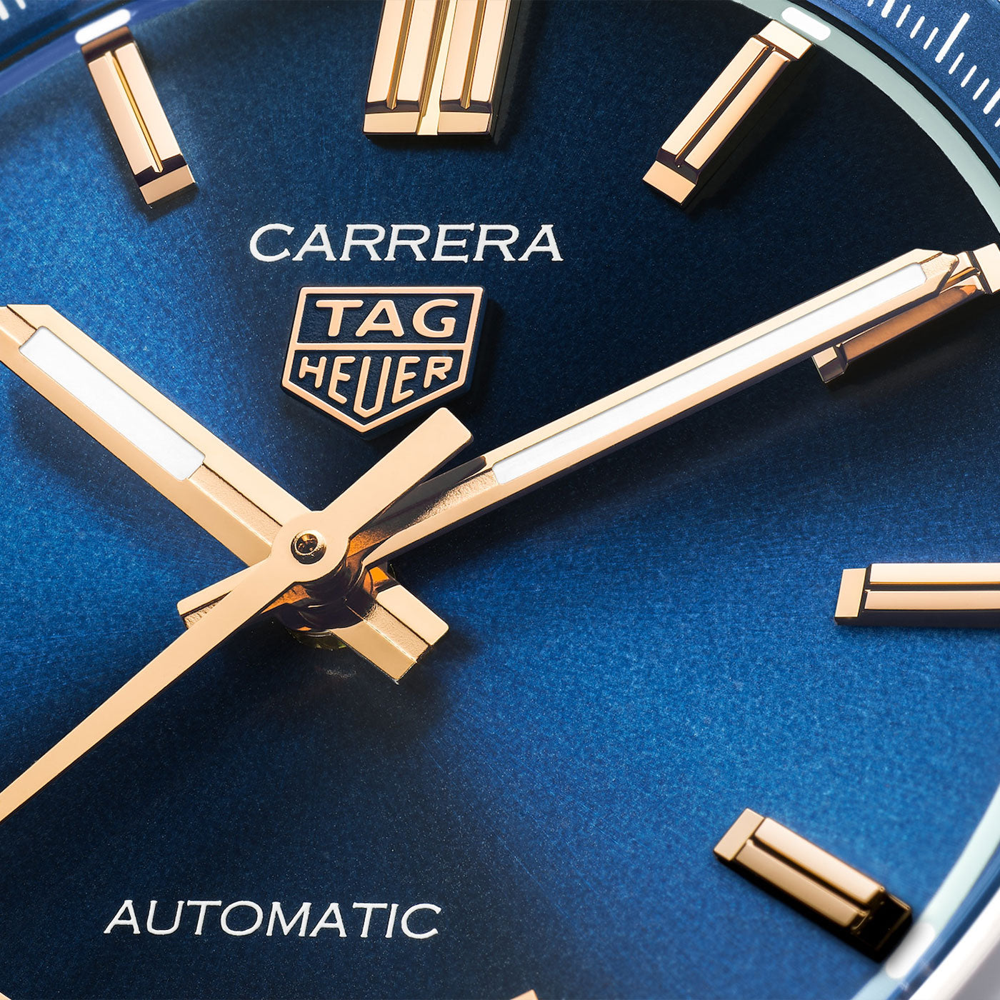 A close-up of the TAG Heuer Carrera Date Automatic 36mm watch face highlights gold hands and markers against a striking blue background, with “CARRERA,” “TAG Heuer,” and “AUTOMATIC” displayed. This sophisticated timepiece from TAG Heuer is powered by the precision Caliber 7 Automatic movement.