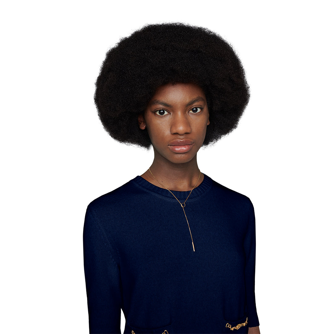 A young woman with a natural afro wears a navy blue top and a GUCCI Fine Jewellery Link To Love 18K Yellow Gold Lariat Necklace, standing against a plain white background.