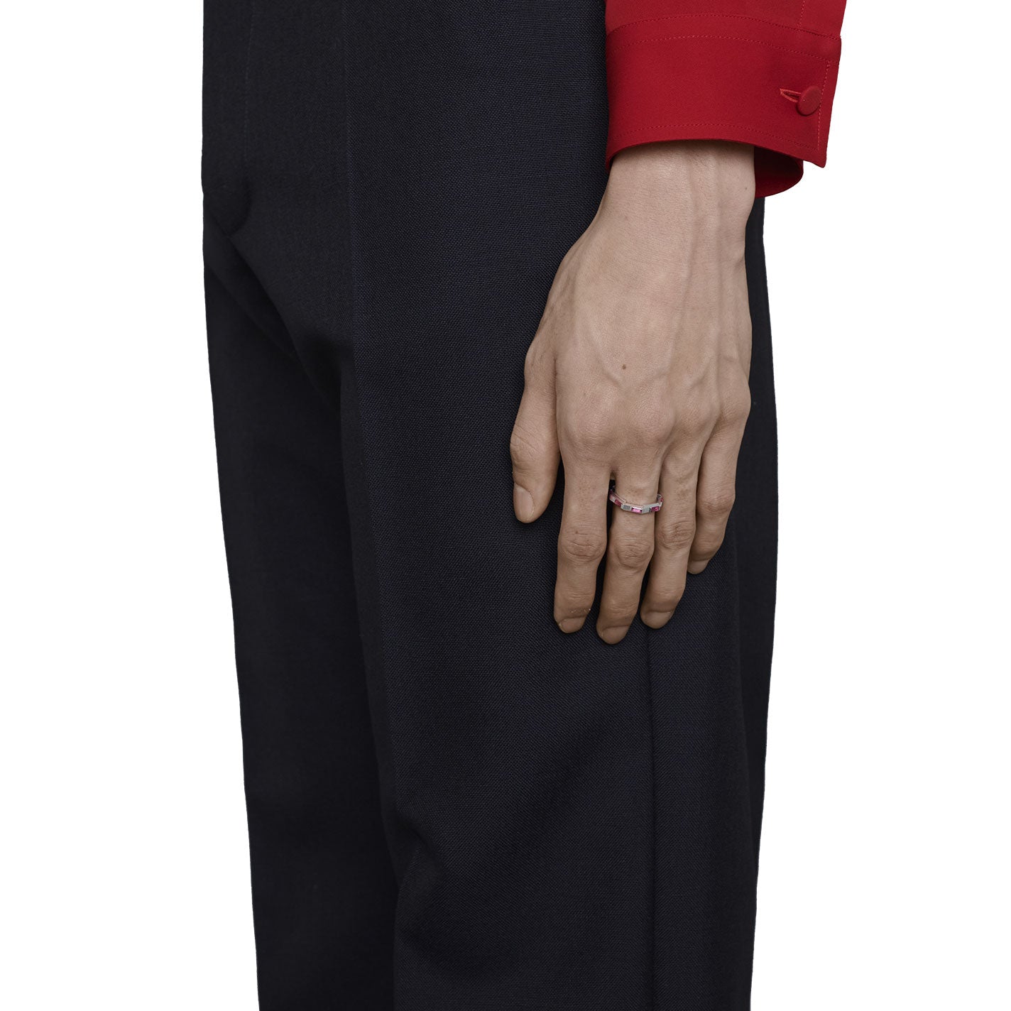 A person in a red long-sleeve shirt and black pants rests their hand against their leg, elegantly showcasing the GUCCI Fine Jewellery Gucci Link to Love Rubellite 18K White Gold Ring. The stunning pink rubellite adorns the ring, while its silver finish gleams against the white background.