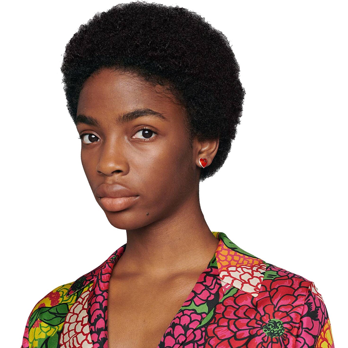 A person with short, curly hair wears a colorful floral-patterned shirt and GUCCI Fine Jewellery's Interlocking G Sterling Silver Stud Earrings adorned with red enamel, looking toward the camera against a white background.