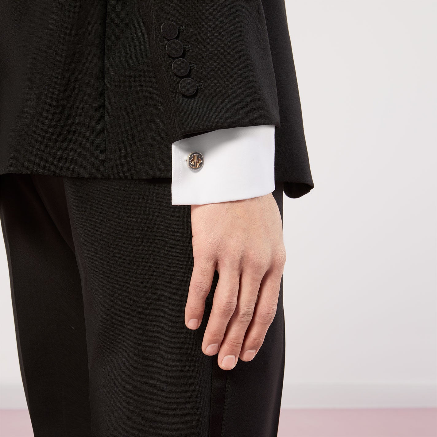 Close-up of a person in a black suit adorned with Gucci Trademark Sterling Silver Cufflinks by GUCCI Gift and Accessories. The individual's hand is relaxed at their side against a neutral background, exuding elegance and grace.