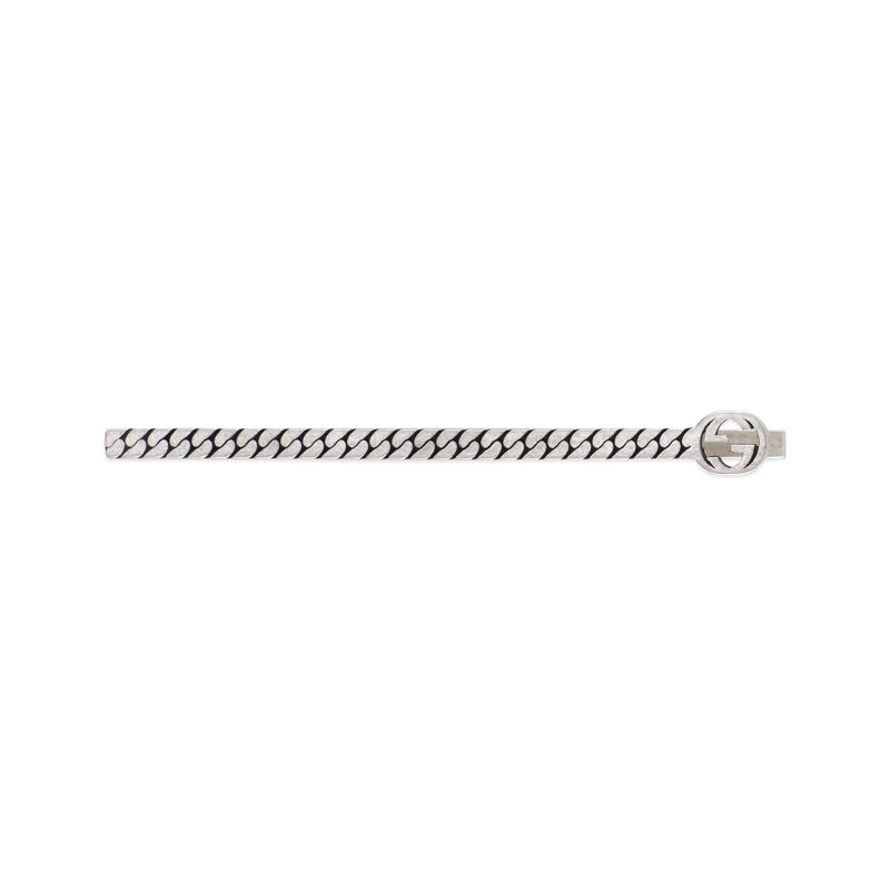 The Gucci Interlocking G Tie Bar by GUCCI Fine Jewellery is a silver accessory featuring a chain-link design and a circular emblem on the right side. This emblem showcases the interlocking G symbol, elegantly merging traditional and modern aesthetics to enhance the sophistication of this sleek piece.