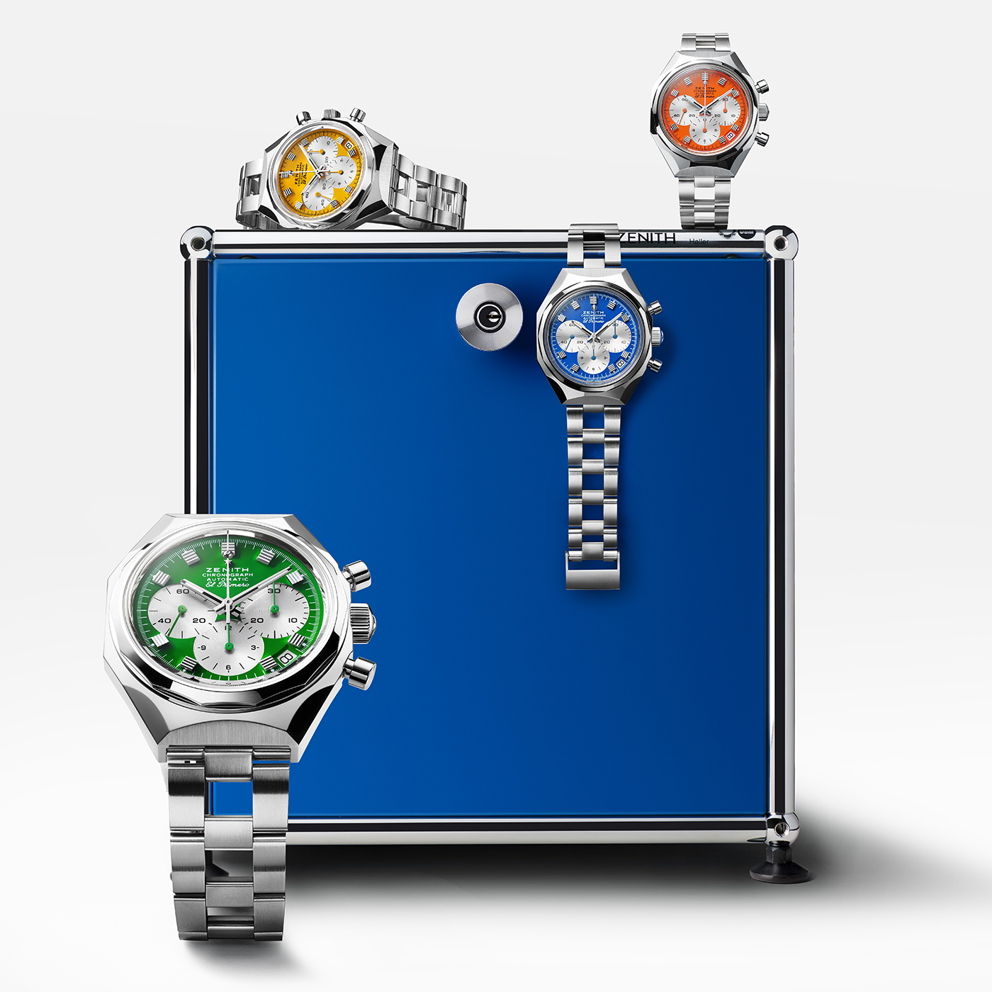 Four Zenith DEFY Chronograph USM - Genetian Blue watches with green, yellow, blue, and orange dials are arranged on and around a metallic blue box. Each features a silver band, octagonal bezel, and bold color accents on a white background.