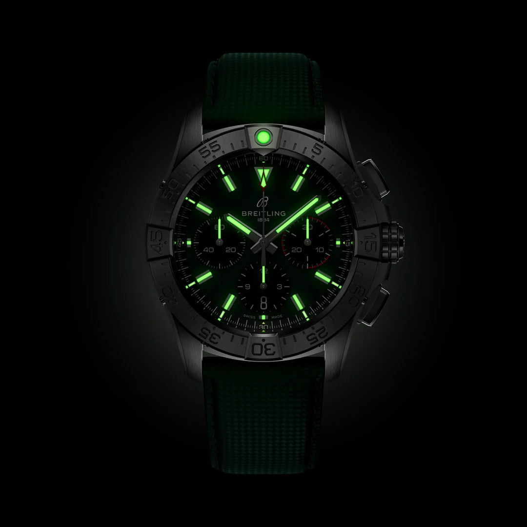 The BREITLING Avenger B01 Chronograph 42 features an aviation-inspired design with a green luminous dial and glow-in-the-dark hands. Its chronograph functions pop against the dark backdrop, complemented by a rugged military leather strap.
