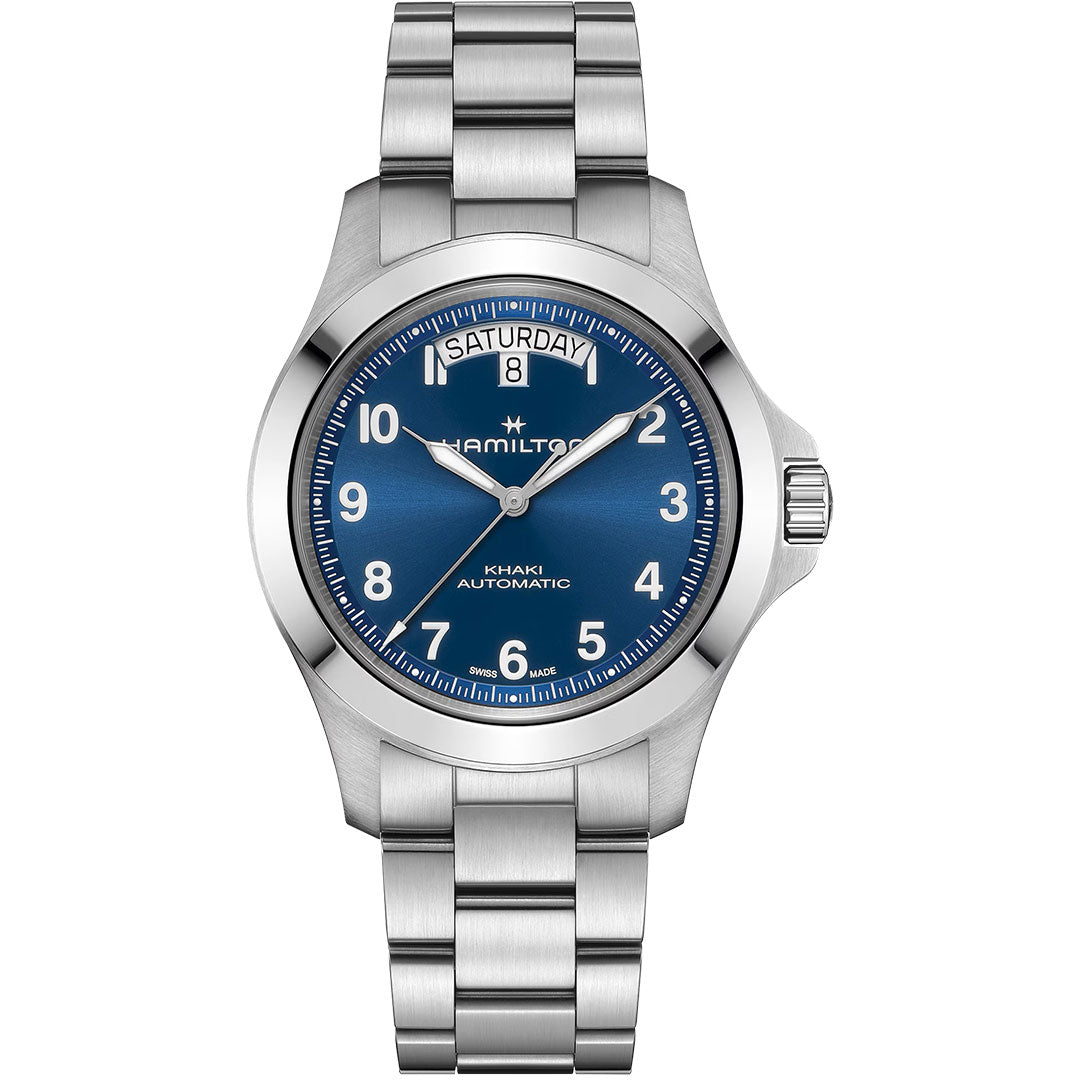 The Hamilton Khaki Field King Auto 40mm Watch by Hamilton Watch features a blue dial with white numerals and hands, day-date display at 12 o’clock, stainless steel case, and a silver metal link bracelet.