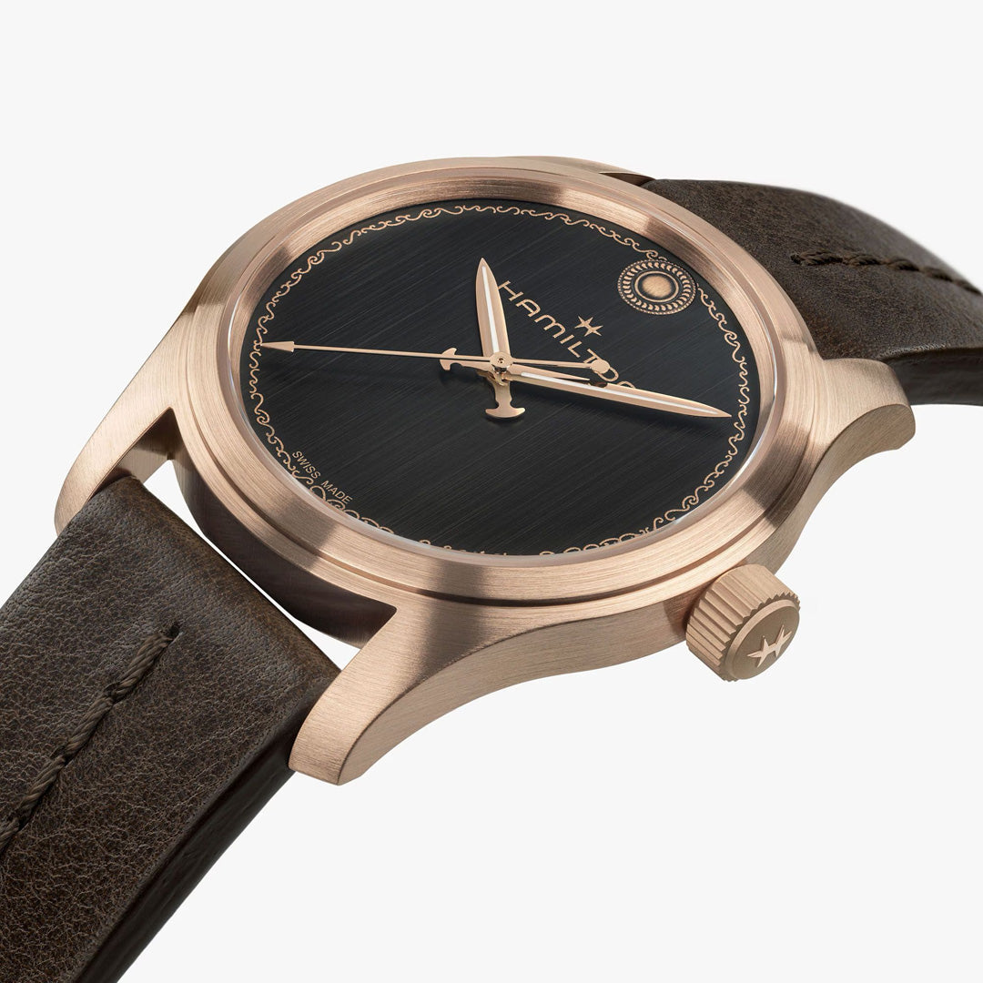 A close-up of the Hamilton Khaki Field The Odyssey Limited Edition Auto 42mm Watch by Hamilton Watch, featuring a bronze case, black dial, gold hands, and a brown leather strap, photographed at an angle against a white background.