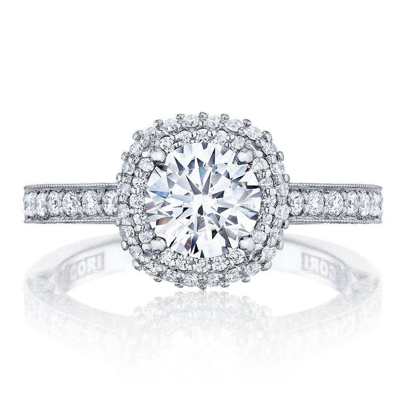 An 18K white gold Tacori Classic Crescent engagement ring showcases a prominent round brilliant diamond at the center, surrounded by smaller diamonds in a halo setting. The band features Signature Crescent detailing adorned with tiny gemstones and is engraved inside with "TACORI.