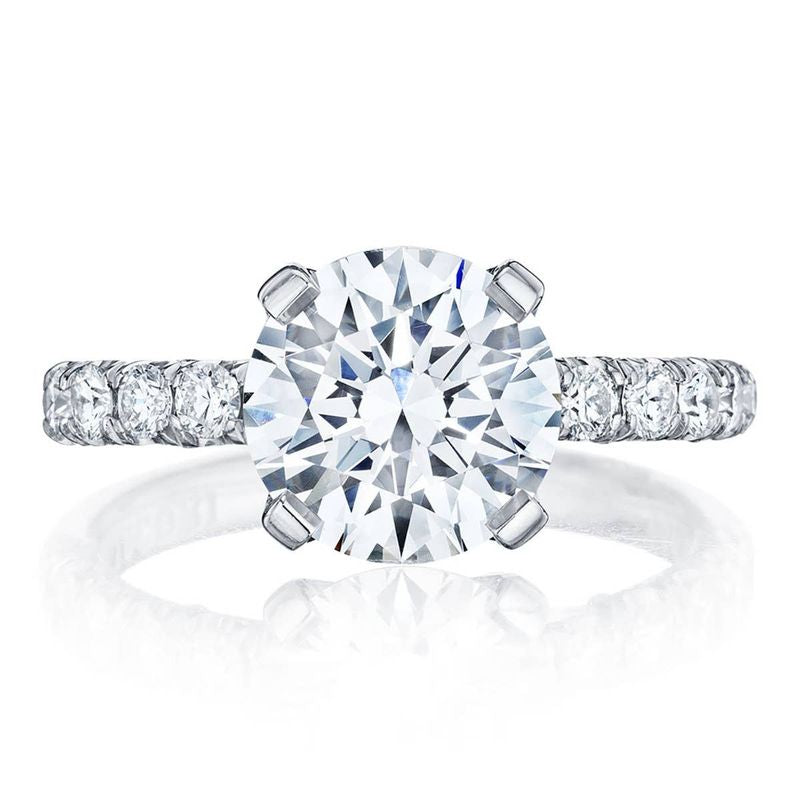 A close-up of the exquisite Tacori Petite Crescent Platinum Round Brilliant Solitaire Semi Mount with Diamond Band showcases a stunning large round diamond in a pronged setting. The band, designed with Tacori's signature Petite Crescent style, is adorned with smaller diamonds that add extra sparkle to this remarkable piece.