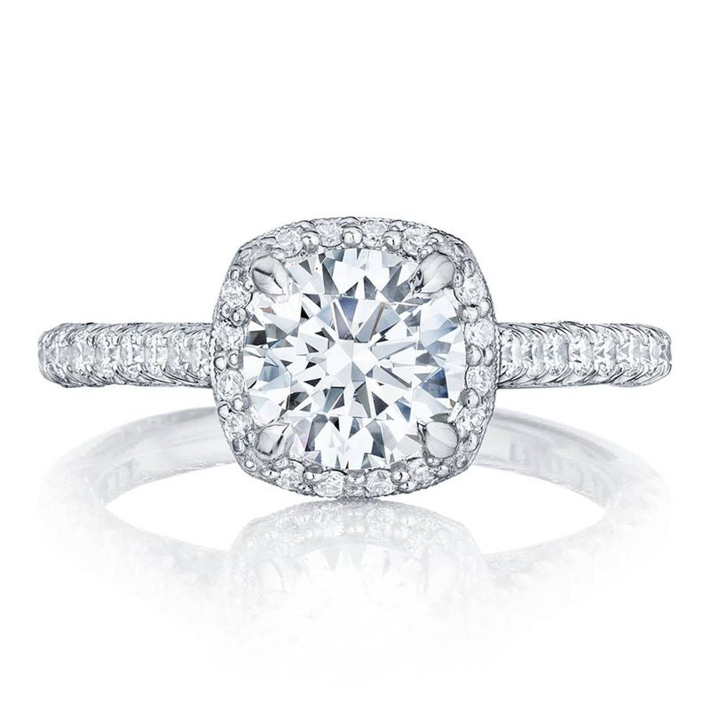 A Tacori Petite Crescent engagement ring in 18K white gold featuring a cushion semi-mount design, highlighted by a diamond halo with smaller diamonds, and a band embellished with additional small diamonds.