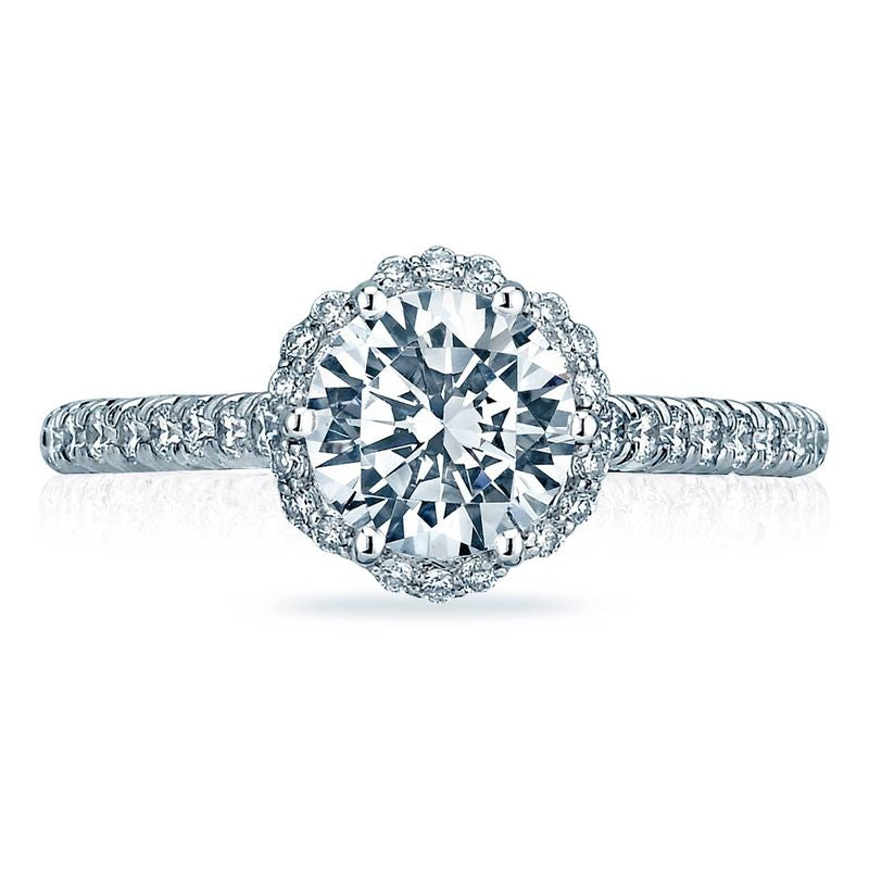 The Tacori Petite Crescent 18K White Gold Round Brilliant Semi Mount Engagement Ring showcases a dazzling design featuring a large round diamond at its center, encircled by a halo of smaller diamonds. The band is adorned with additional small diamonds, creating an intricate and sparkling look characteristic of the Petite Crescent style.