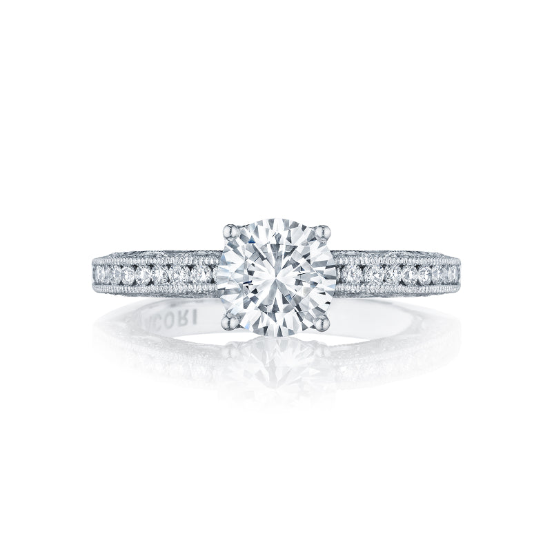 An 18K white gold engagement ring from Tacori, known as the Classic Crescent Round Brilliant Solitaire Semi Mount, showcases a large round diamond at its center with smaller diamonds elegantly embedded along the delicate band, set beautifully against a white background.
