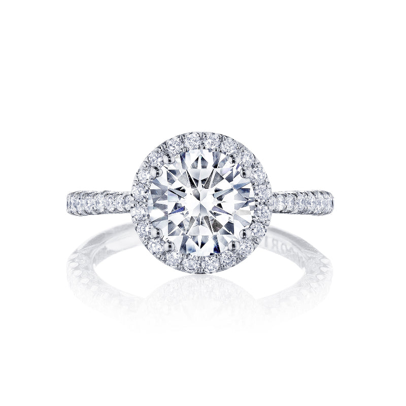 The Tacori Petite Crescent 18K White Gold Round Brilliant Semi Mount with Diamond Band and Halo Engagement Ring showcases a round central diamond encircled by a halo of smaller diamonds. Crafted with precision, the band is adorned with additional diamonds, enhancing the ring's sparkle and elegance.