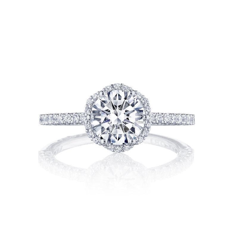 This Tacori Petite Crescent 18K White Gold Round Brilliant Semi Mount with Diamond Band and Halo Engagement Ring showcases a central round diamond surrounded by a halo of smaller diamonds. The band, adorned with diamonds, enhances its shine against a white background, making this piece truly exquisite.