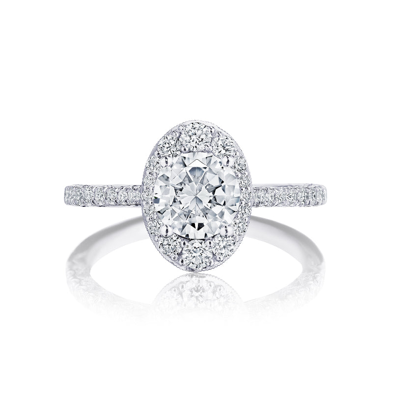 This elegant Tacori Petite Crescent engagement ring in 18K white gold showcases a stunning round brilliant diamond at the center, encircled by a halo of smaller diamonds. The band, crafted by Tacori gemologists, features delicate diamonds and a crescent design embellished with additional diamonds for an opulent and sparkling look.