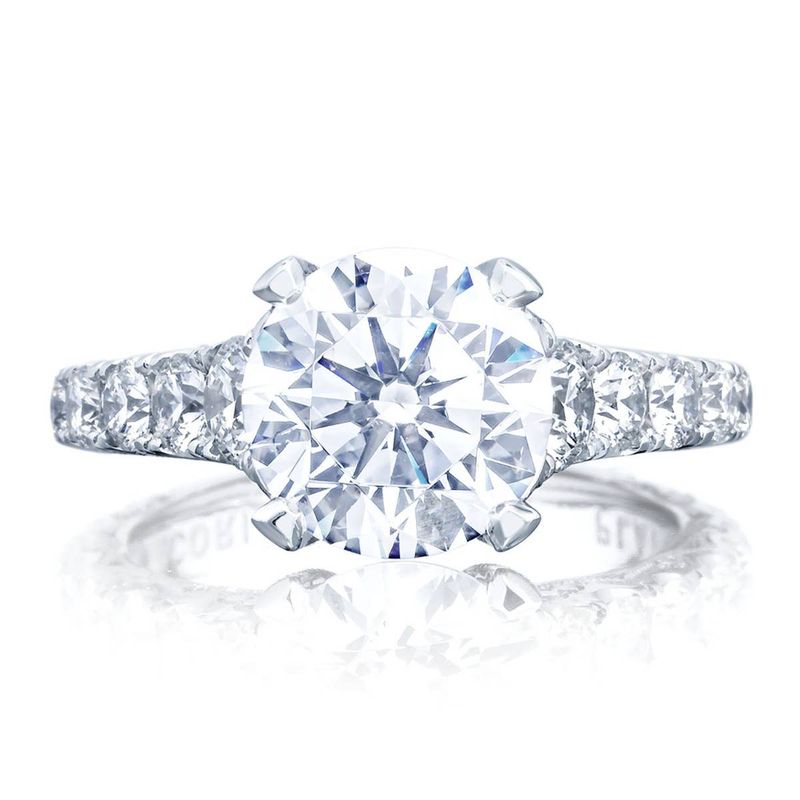 The Tacori Petite Crescent RoyalT Platinum Round Brilliant Solitaire Semi Mount Engagement Ring showcases a prominent round center stone in a classic prong setting. The elegantly designed band, featuring Tacori's signature hidden bloom pattern, is adorned with smaller diamonds, offering an exquisite look. Set against a white background, this piece from Tacori exudes timeless beauty.