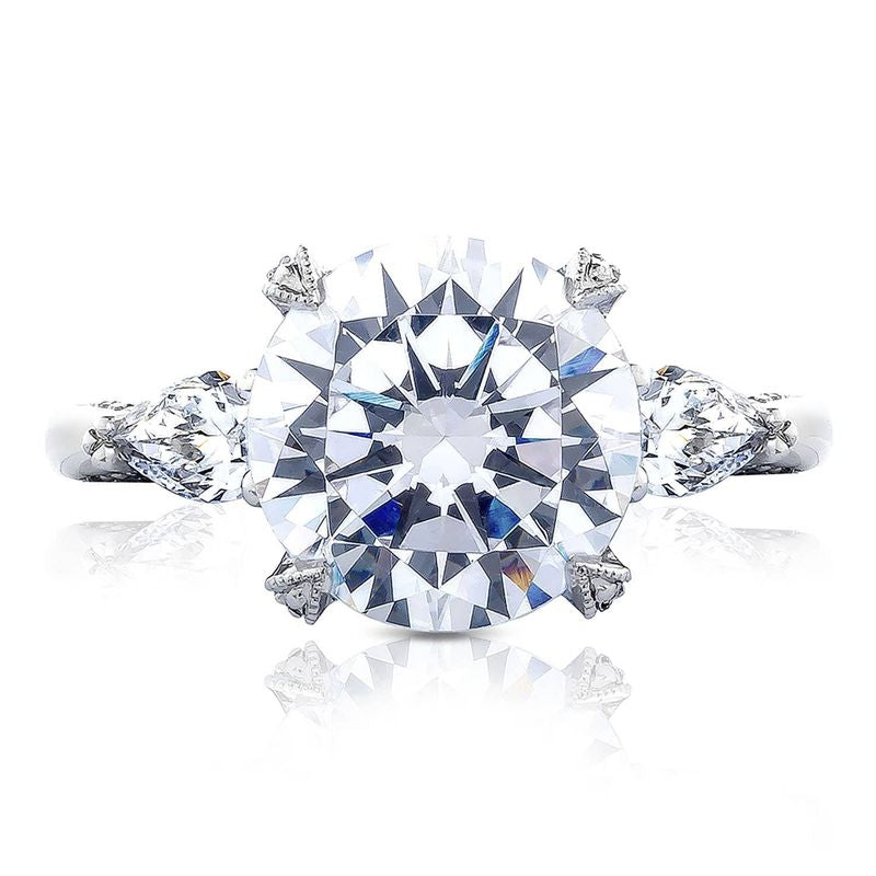 A close-up of the sophisticated Tacori Simply Tacori RoyalT Platinum engagement ring showcases a central round brilliant diamond, accented by smaller pear-shaped diamonds on a sleek platinum band, set against a pristine white background.