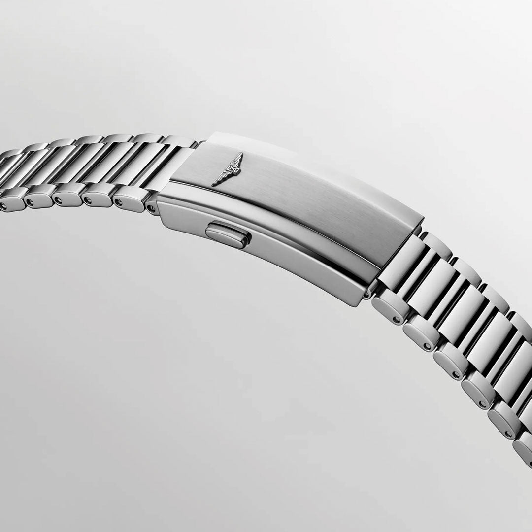 A close-up of the Longines Conquest Heritage Automatic 38mm watch shows its silver metal bracelet with a clasp engraved with the Longines winged logo, highlighting the vintage design against a plain light gray background.