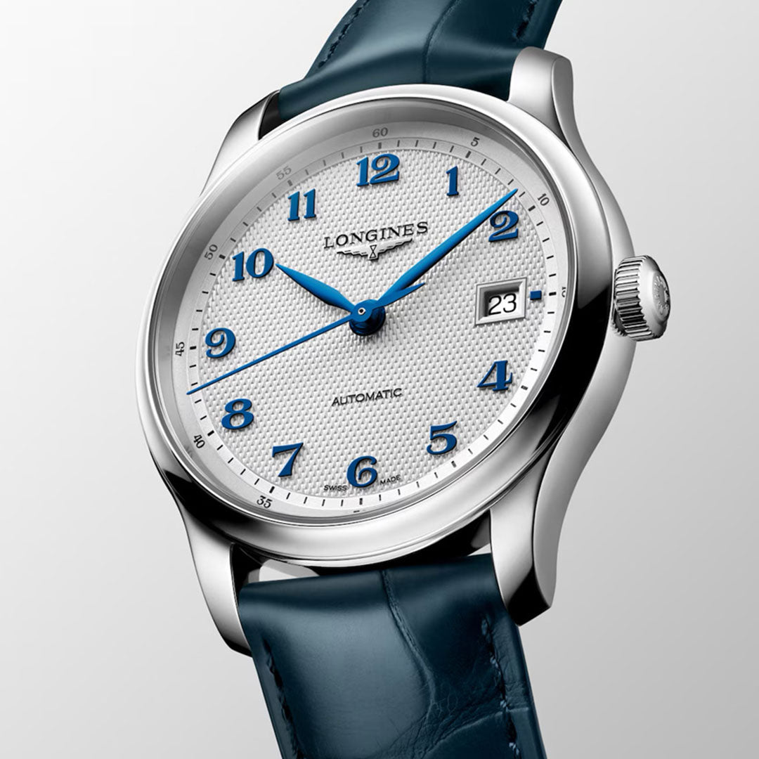 The Longines Master Collection Automatic 39mm Watch features a textured white dial, blue hands and Arabic numerals, date at 3 o’clock, and a blue leather strap—exemplifying Longines craftsmanship against a light gray background.