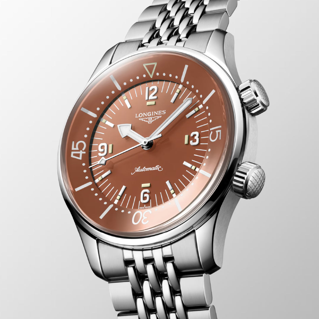 The Longines Legend Diver Automatic 39mm Watch features a stainless steel finish with a vintage brown dial, silver hour markers, two crowns, and a date display. "Longines" and "Automatic" adorn the light gradient background, complemented by a steel bracelet.