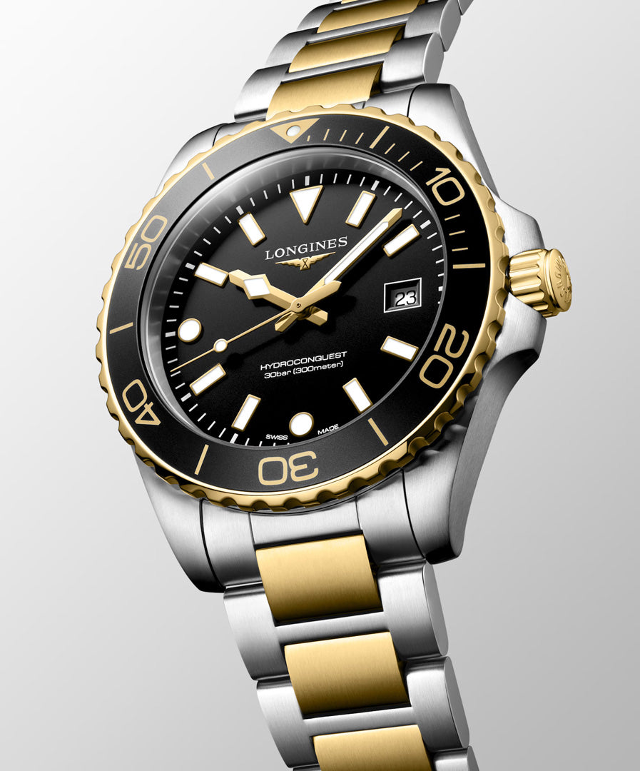 A close-up of a Longines HydroConquest Quartz 42mm Watch, featuring a black dial, gold bezel, and two-tone gold and silver metal bracelet, displayed at an angle on a light background—an elegant Swiss timepiece by Longines inspired by iconic sport watches.