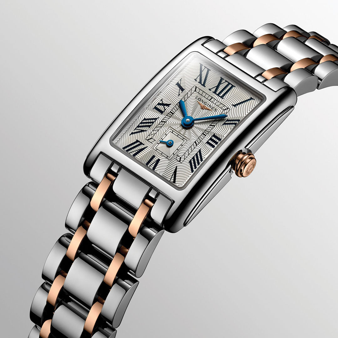 A close-up of the Longines Dolcevita Quartz 20.8 x 32mm watch features a rectangular case, blue hands, Roman numerals, and a two-tone silver and rose gold bracelet against a light gray backdrop.