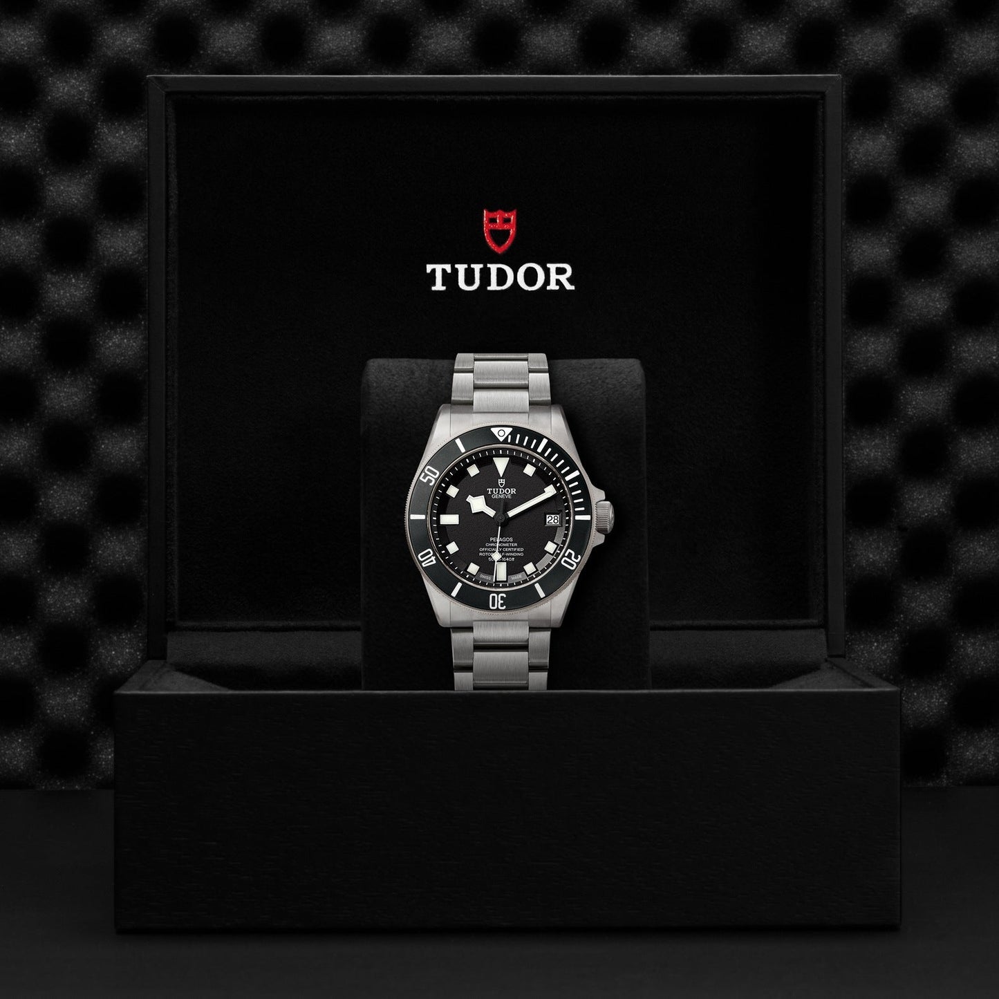 A TUDOR Pelagos divers' wristwatch, featuring a sleek silver metal strap and black dial, is presented in its sophisticated black box. The inside of the lid displays the TUDOR logo in red and white, emphasizing its 500m waterproof capability for assured underwater adventures.