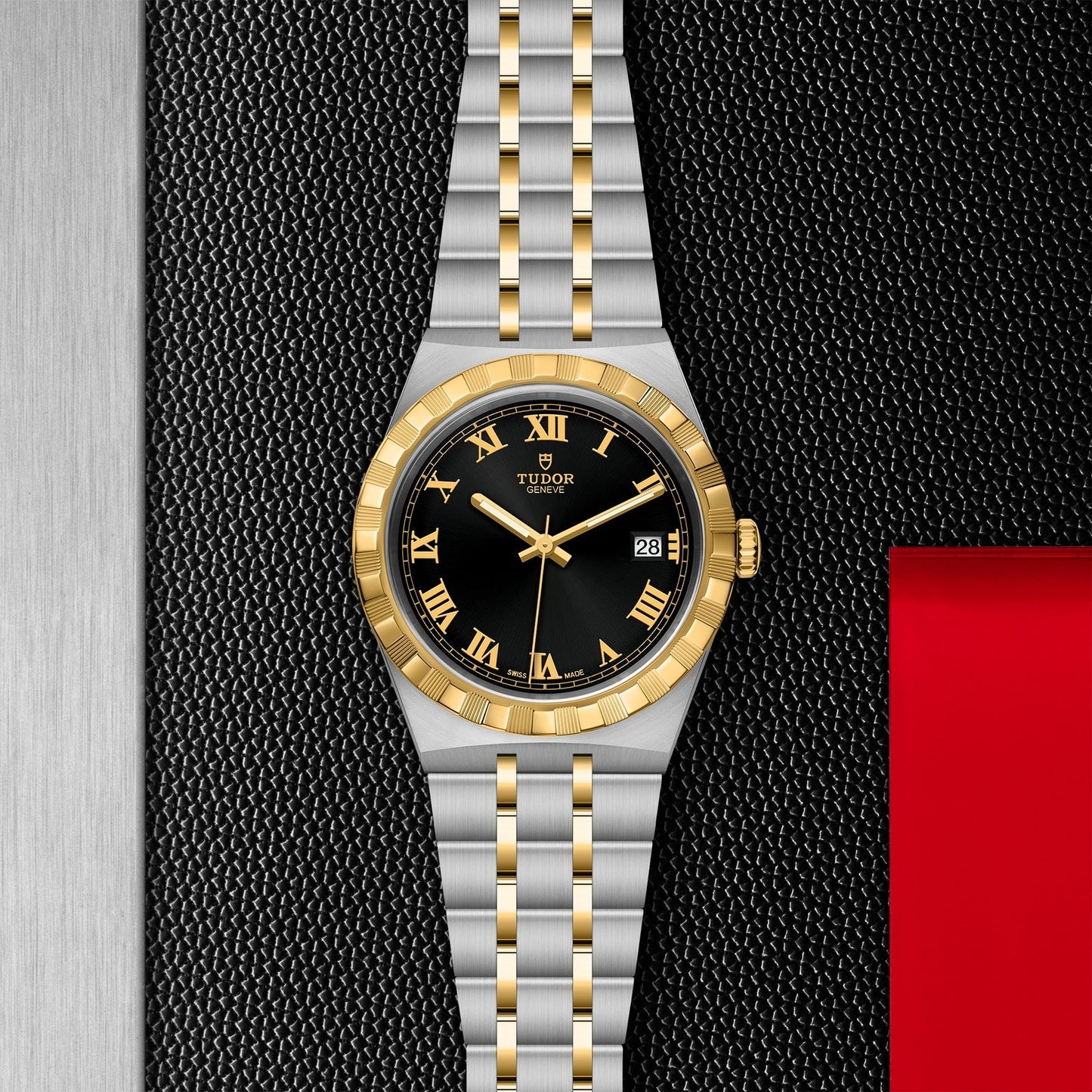 The TUDOR Royal from TUDOR showcases a sport-chic elegance with its two-tone gold and silver bracelet. This automatic timepiece features a black dial adorned with gold Roman numerals and hands, set against a textured backdrop that combines black and metallic hues, highlighted by a subtle red accent.