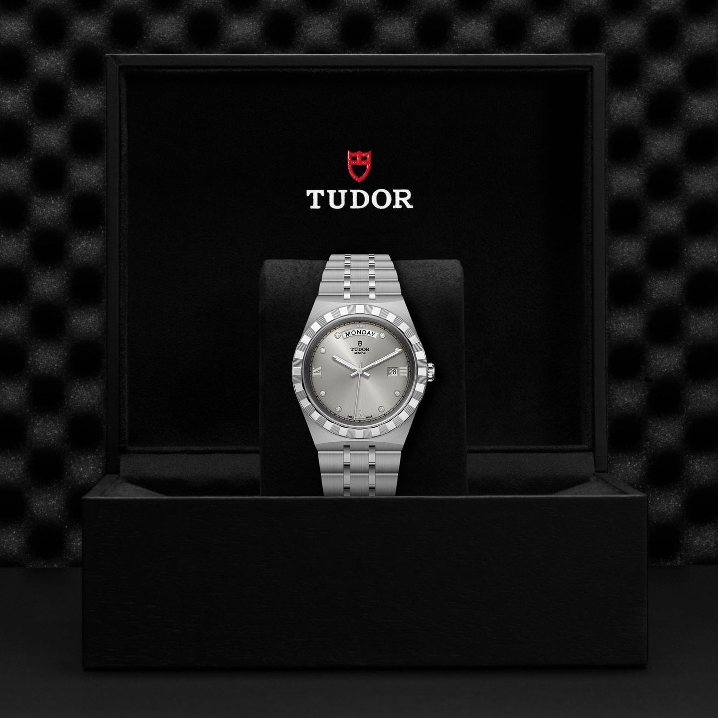 A TUDOR Royal watch rests elegantly in an open black box, featuring a stainless steel and gold strap. The light dial highlights minimalist design elements, while the TUDOR logo is prominently displayed on the inside lid of the box, epitomizing automatic sport-chic watches.