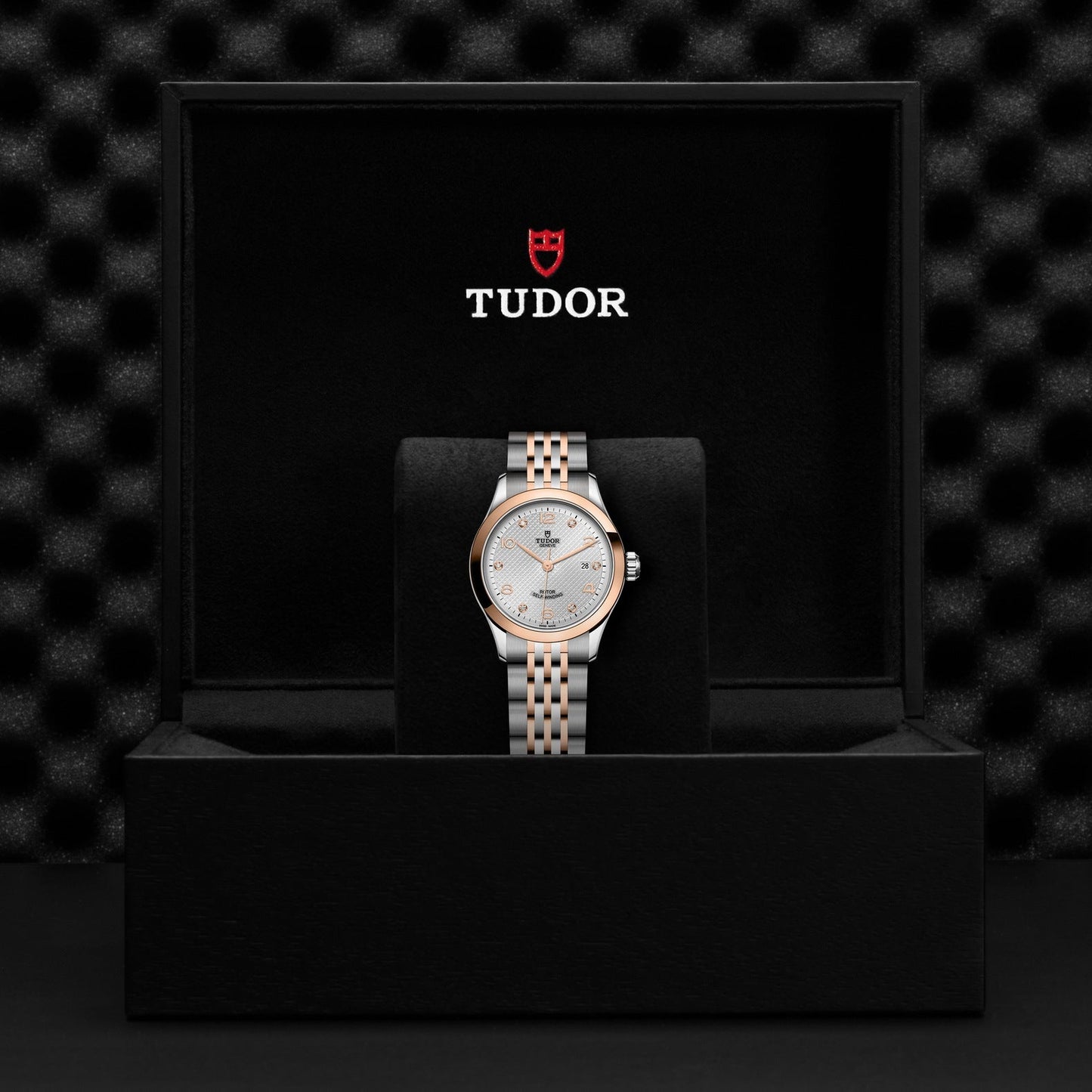 A TUDOR 1926 watch, featuring a diamond-set dial, is presented in an open black box with the iconic TUDOR logo. The watch exhibits a silver face, gold and silver hour markers, and a two-tone silver and gold bracelet. The interior of the box flaunts a textured black surface.