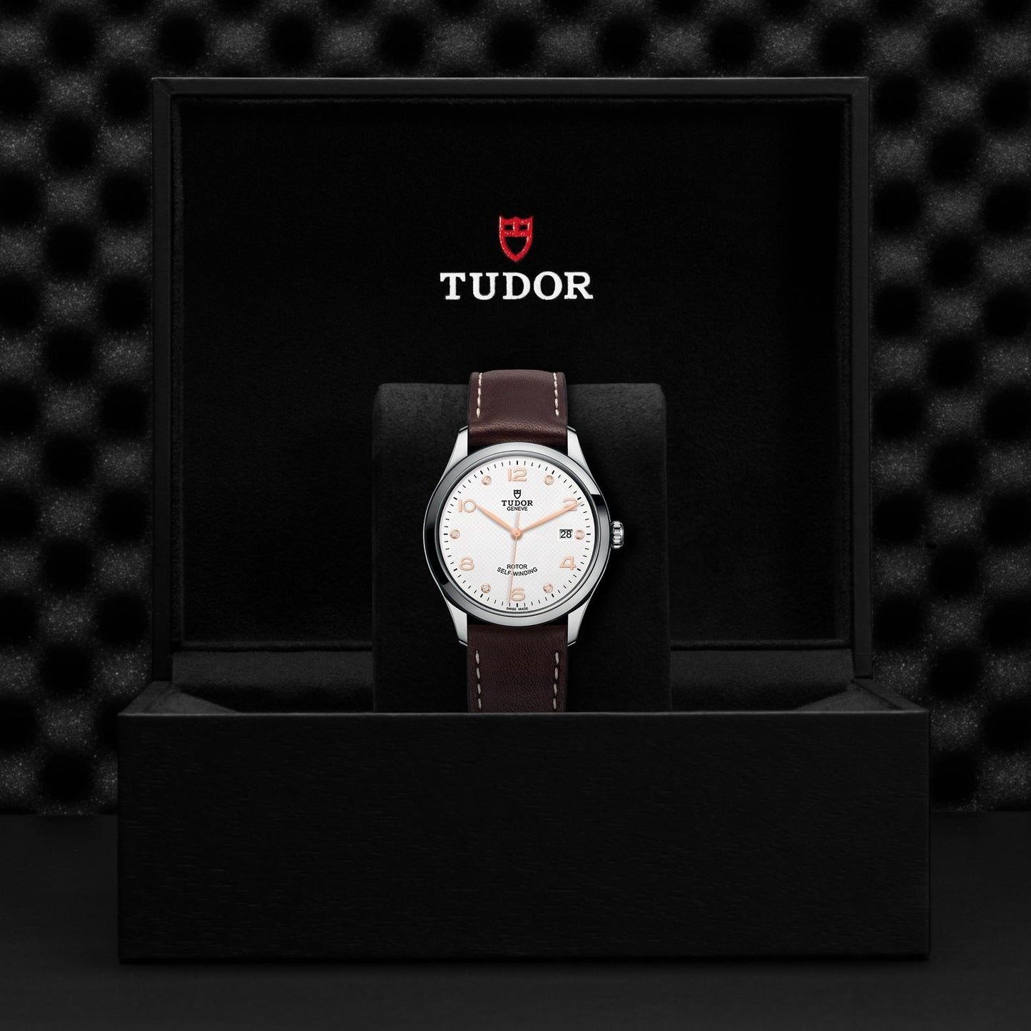 The New Old Stock TUDO1 1926 wristwatch showcases a white face, brown leather strap, silver hour markers, date window at 3 o'clock, and the iconic Tudor logo. It is elegantly presented in an open black box.