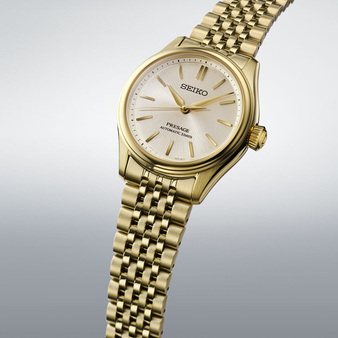 The Seiko Presage Classic Series Automatic With Manual Winding 41mm Watch features a gold case, white dial, gold hour markers, and matching gold link bracelet, displayed on a gradient light gray background.