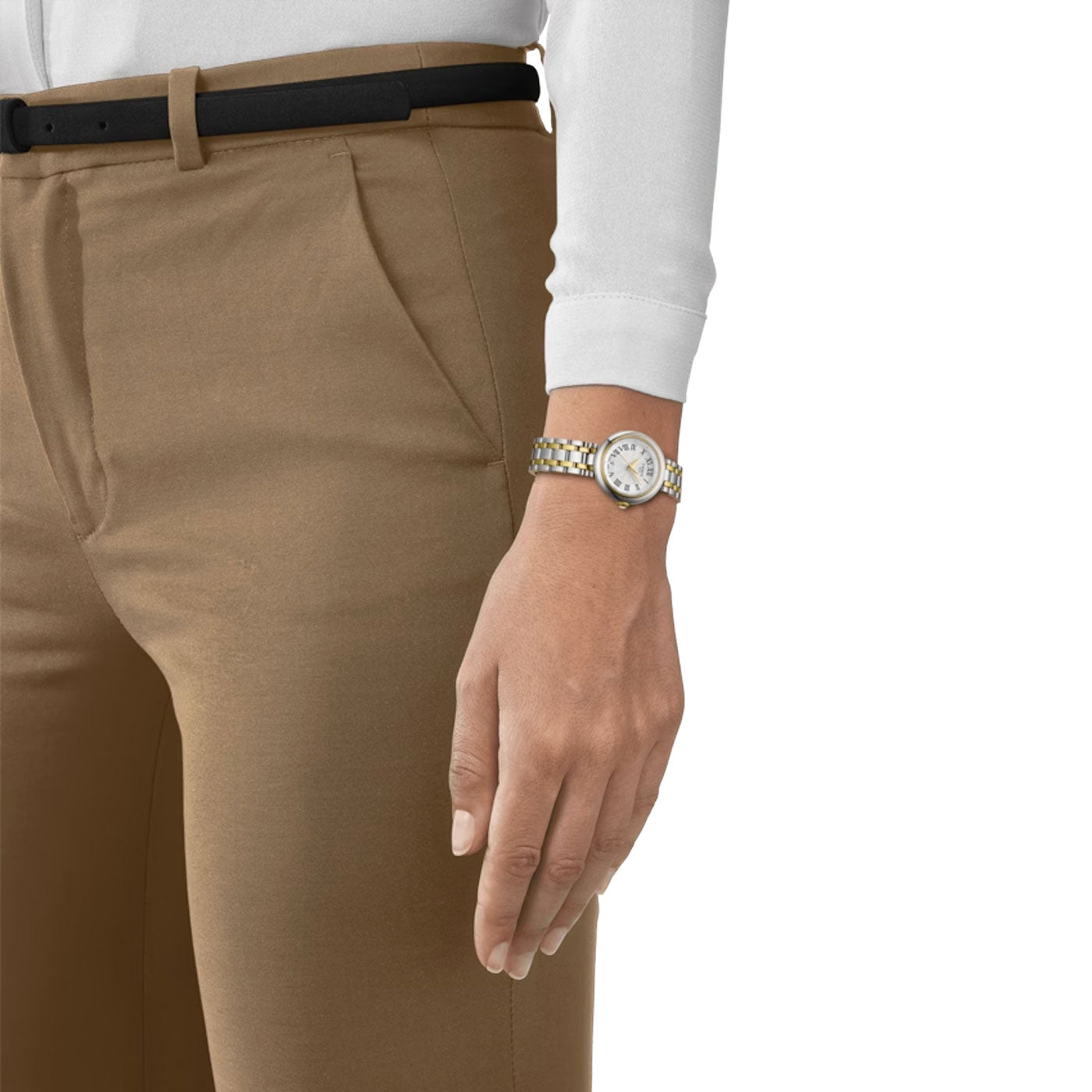 A person dressed in brown trousers, a white long-sleeve shirt, and a black belt showcases the Tissot Bellissima Small Lady Quartz 26mm Watch on their left wrist, known for its Swiss Quartz Movement and Scratch-Resistant Sapphire Crystal. Their arm hangs relaxed by their side against a white background.