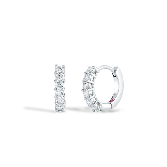 A pair of Roberto Coin Perfect Diamond 18K White Gold Huggie Diamond Earrings exudes elegance, featuring a shimmering row of diamonds. One earring stands upright while the other lies flat against a soft white background, showcasing their stunning craftsmanship.