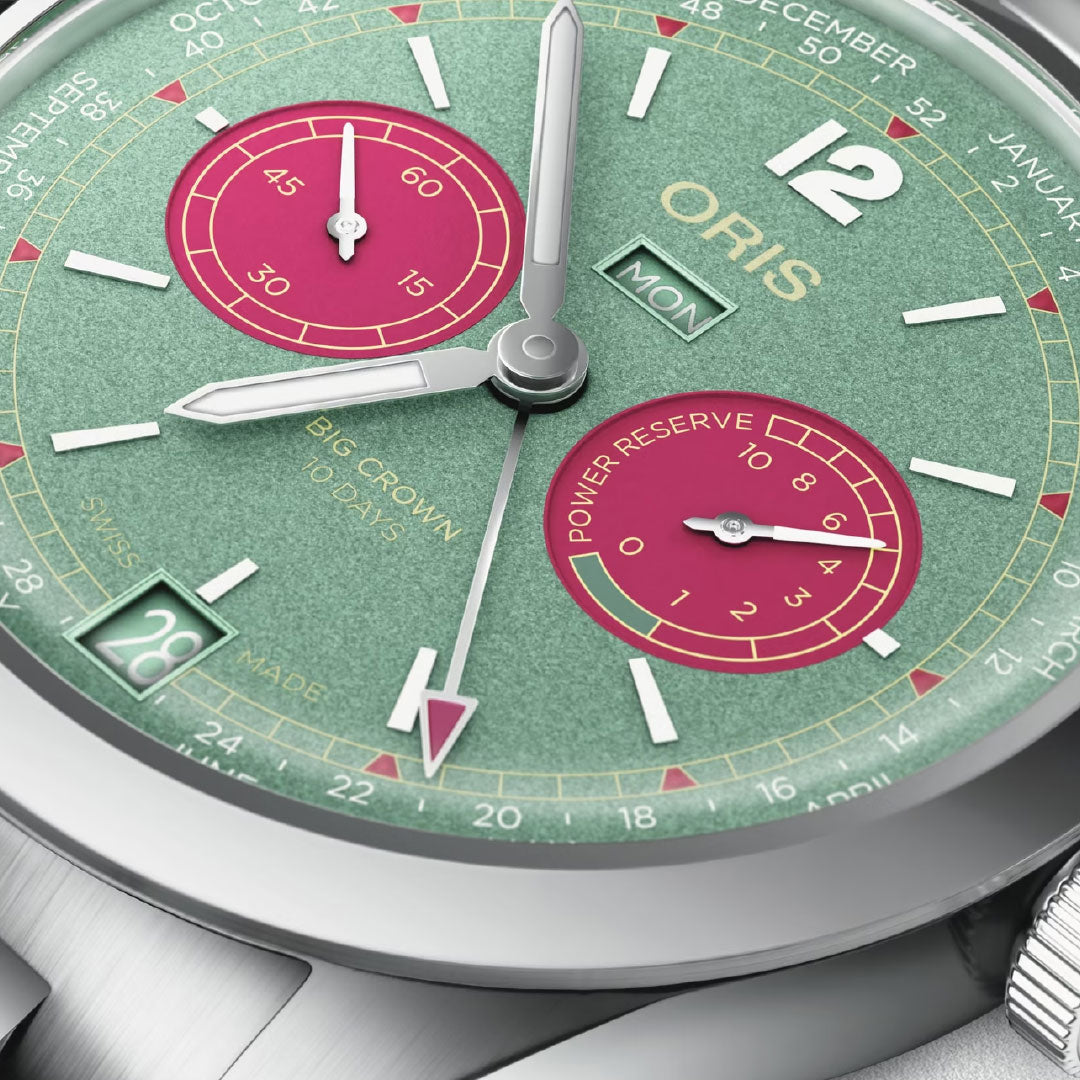 Close-up of the ORIS Big Crown Calibre 113 Automatic Winding 43mm watch, featuring a green dial with pink subdials, silver hands, business calendar, date at 6 o’clock, power reserve display, and day window at 3 o’clock.