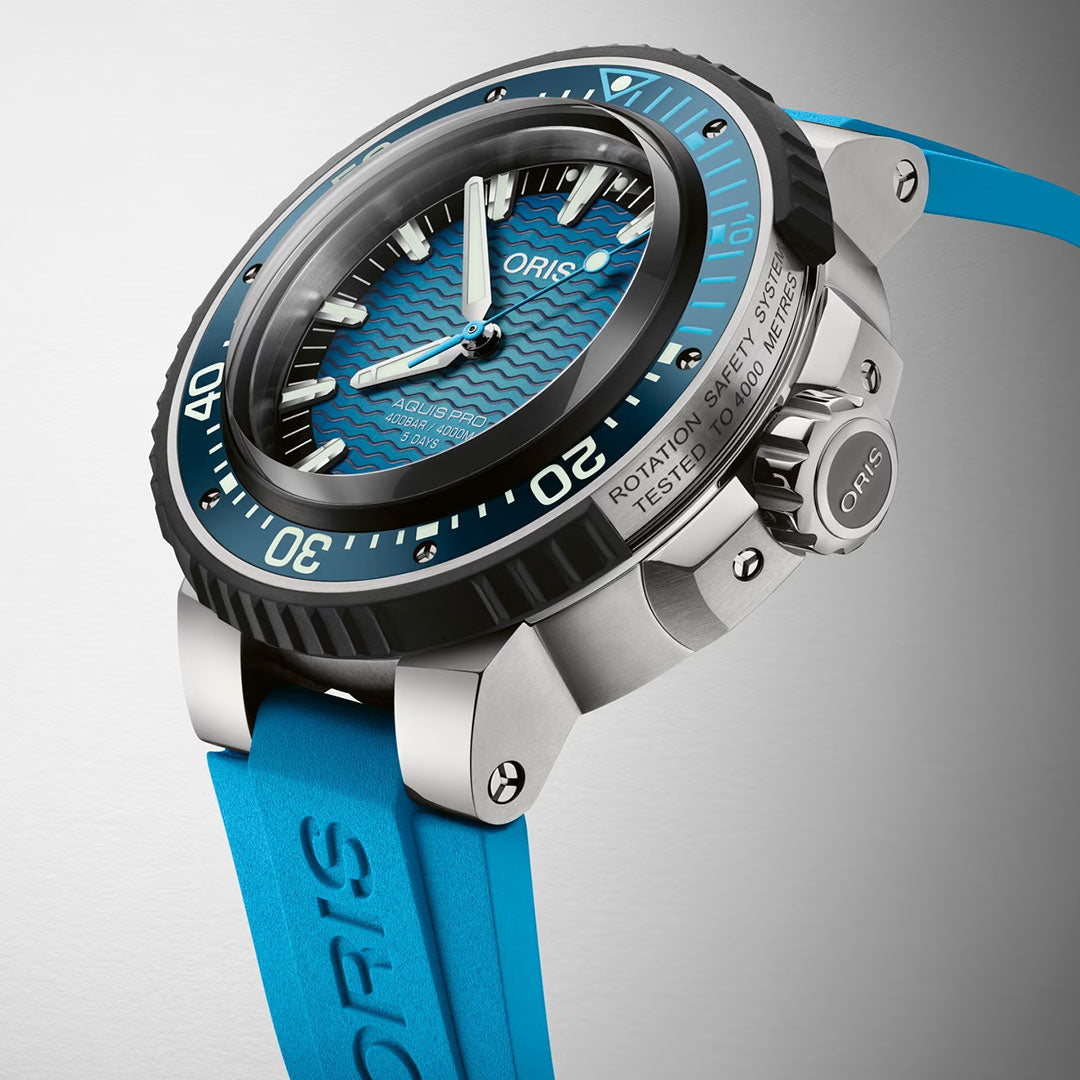 A close-up of the ORIS Aquis Pro 4000m Automatic Winding 49.5mm Watch, featuring a blue strap, textured blue dial, black bezel, and white markers, displayed at an angle on a light gray background. This advanced ORIS timepiece offers remarkable water resistance up to 4000 metres.