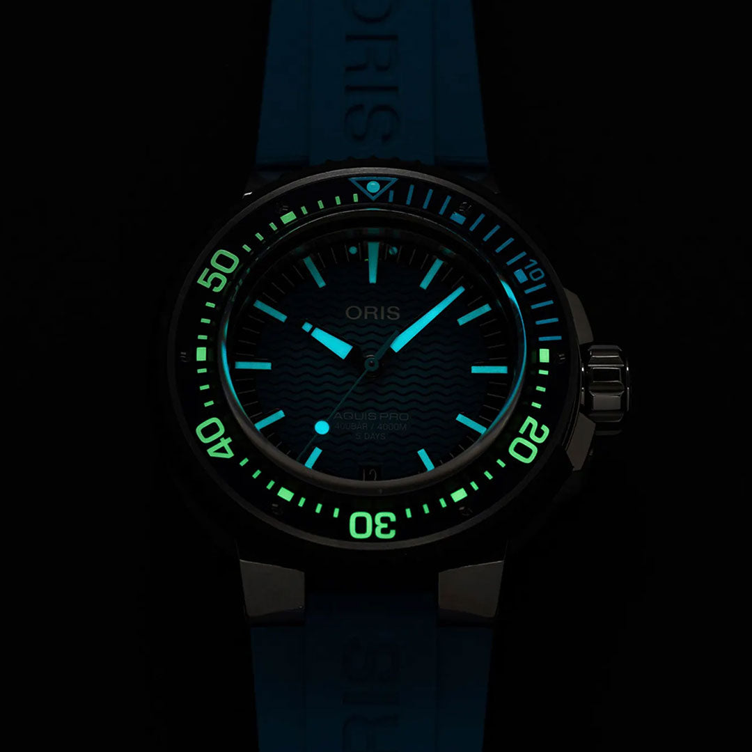 The ORIS Aquis Pro 4000m Automatic Winding 49.5mm Watch features luminescent blue hour markers and hands, complemented by a green minute track on the bezel. Designed for serious divers, this watch boasts remarkable water resistance and is paired with a striking blue strap that contrasts against its black case—making the Oris Aquis Pro 4000m an ideal choice for underwater exploration.
