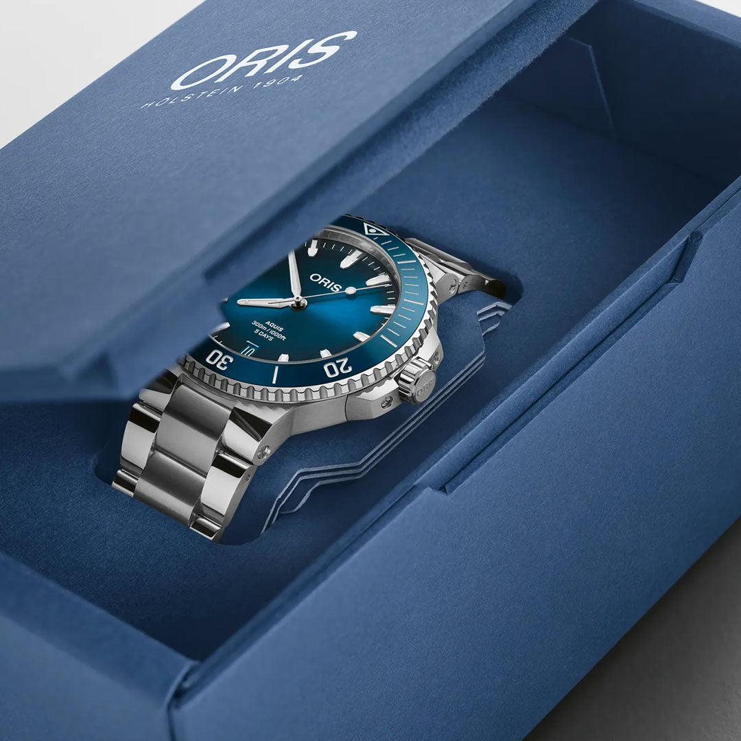 An ORIS Aquis Date Calibre 400 Automatic 43.5mm watch with a blue dial and metal band is shown in an open blue ORIS box, partially out of the packaging, highlighting its luxury toolwatch design and branding.