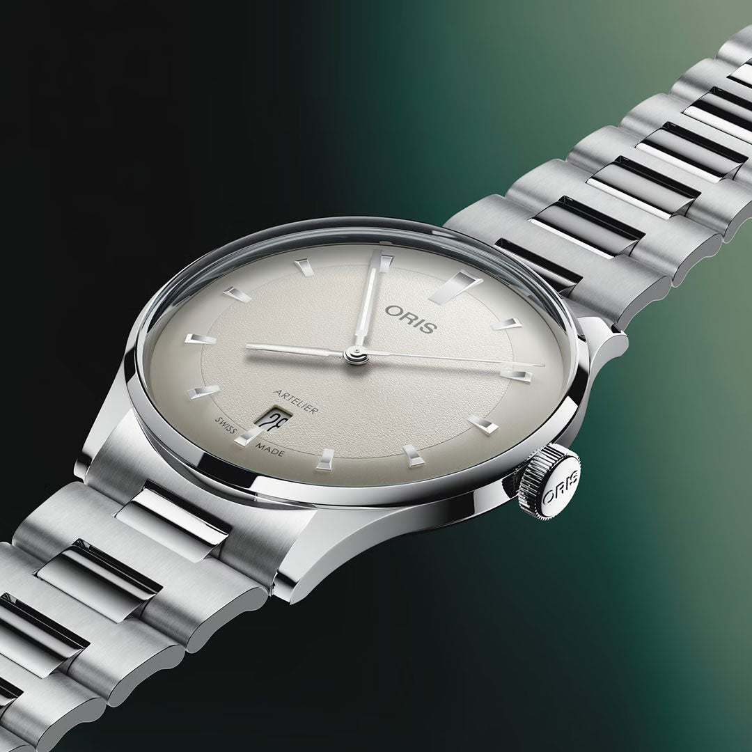 The ORIS Artelier Date Calibre 733-1 Automatic 38mm watch features a silver-tone design, metal bracelet, cream dial with silver markers, and date at 6 o’clock. Swiss made, displayed on a black and green gradient background.