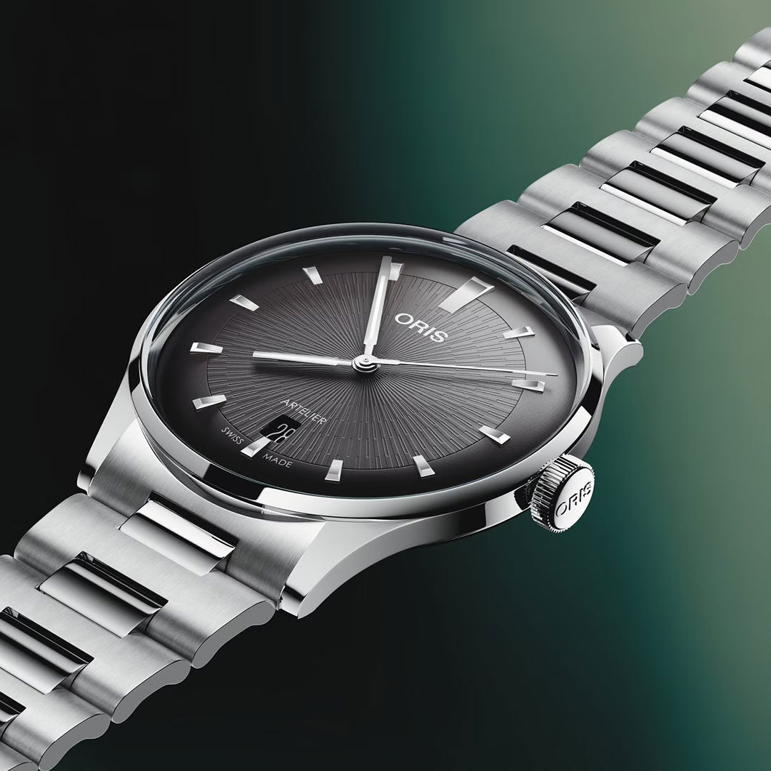 A close-up of the ORIS Artelier Date Calibre 733-1 Automatic 38mm Watch, featuring a sunray black dial, silver markers, and metal bracelet, set against a green-black gradient. This Swiss Made timepiece by ORIS epitomizes timeless elegance.