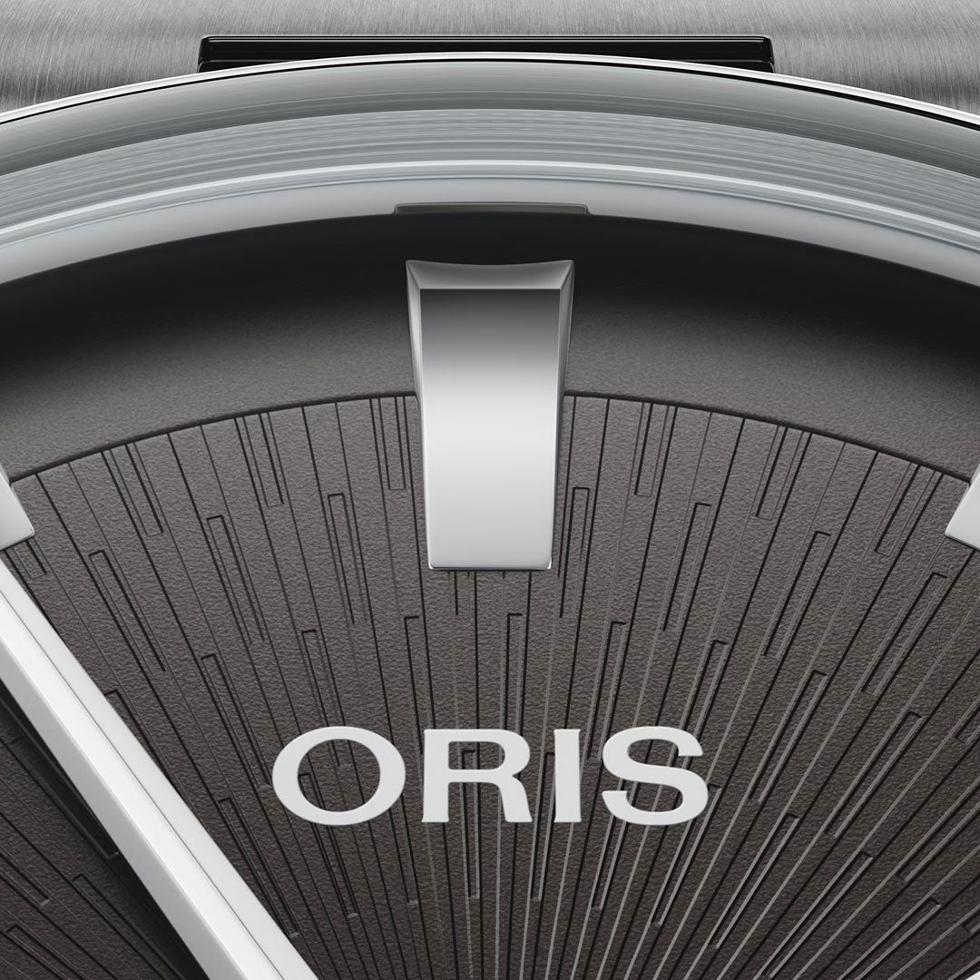 Close-up of the ORIS Artelier Date Calibre 733-1 Automatic 38mm Watch face with a textured dark background, bold silver hour marker, "ORIS" in white letters below, and partially visible Swiss Made mechanical hands.