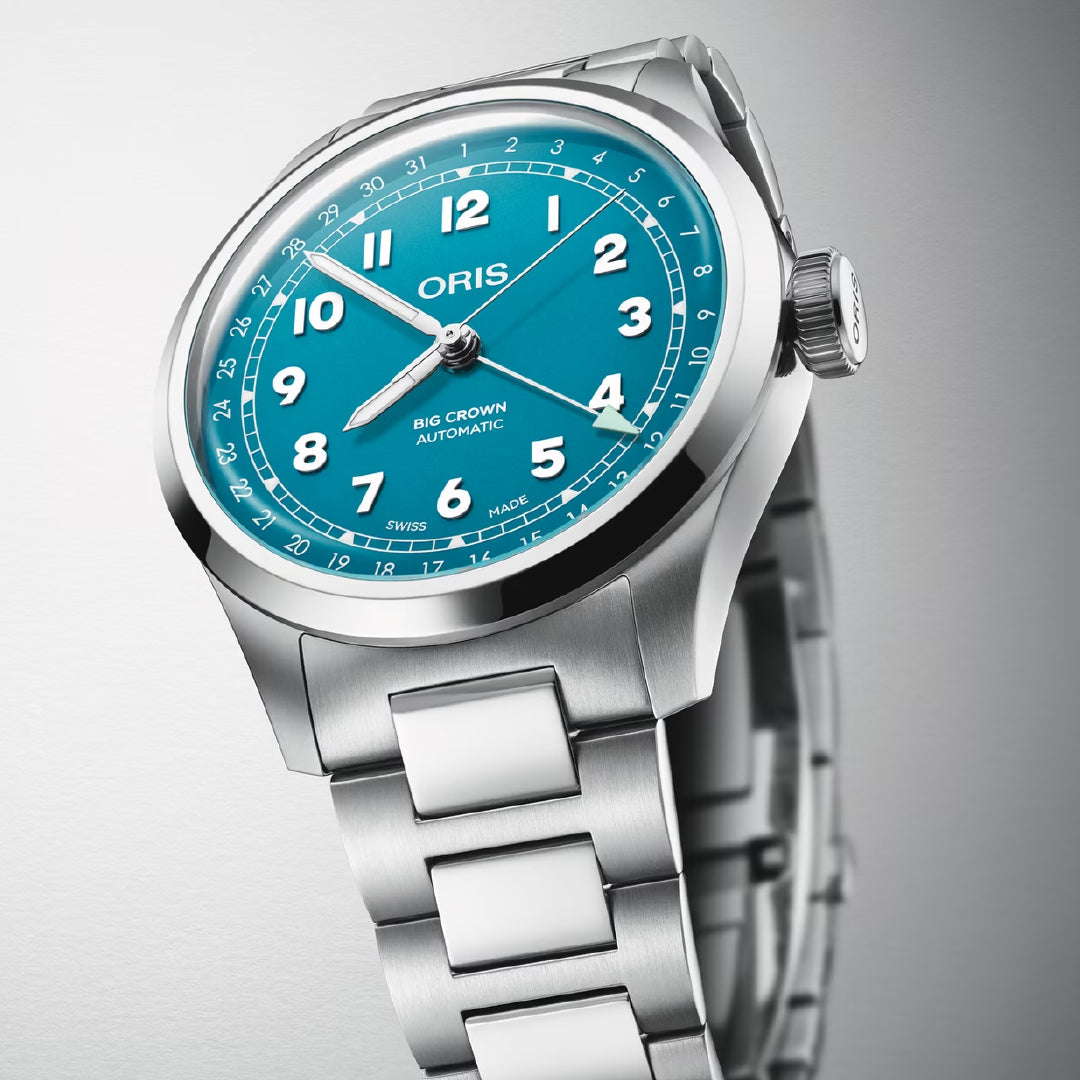 The ORIS Big Crown Pointer Date Calibre 754-1 Automatic Winding 40mm watch features a turquoise blue dial with white numerals, date window, metal bracelet, and Swiss Made movement, shown angled on a light grey background.